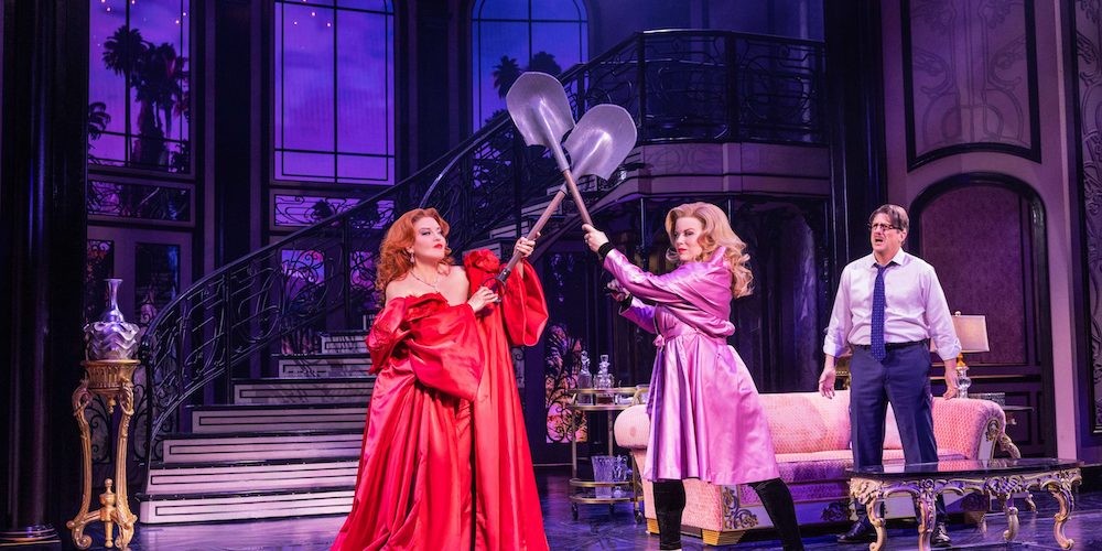 Two women in elaborate dresses fight with shovels on a stage. 