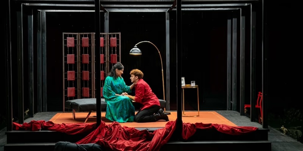 A man and woman on a stage made to look like a living room. 