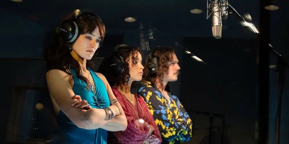 Three people wearing headphones and standing in front of microphones. 