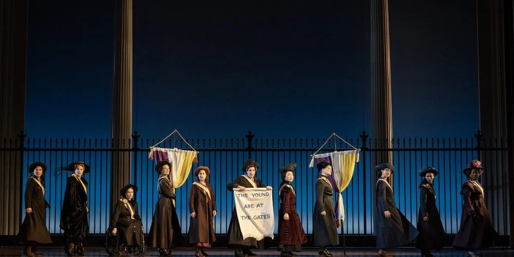Women in historic costumes and banners on a stage.