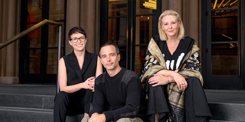 Three people sit on steps of a building. 