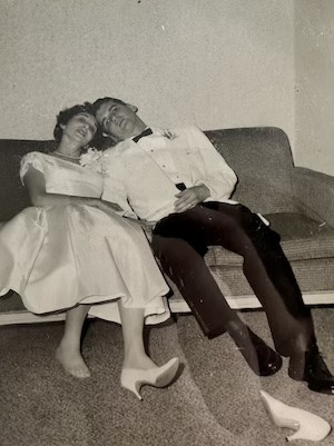 Joan Rubinstein and Leonard Freeman in wedding clothes sitting on a couch.