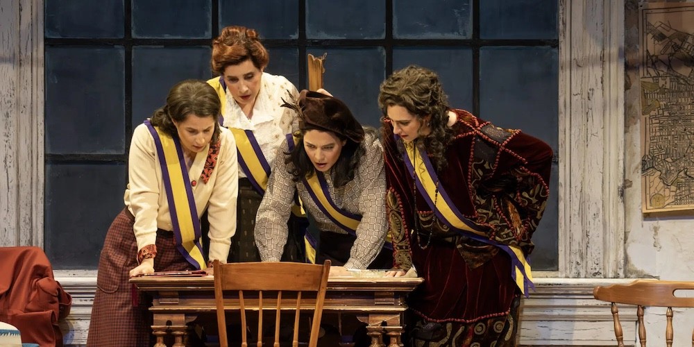 Four women looking at items on a desk. 