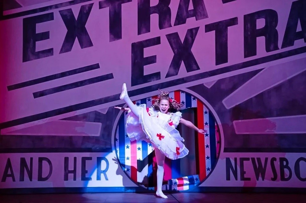 Actor in white dress high kicks center stage. 