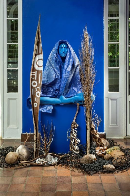 Origins of Devotions (Installation Detail), Dimensions Variable, Plaster, Blue Hurricane tarp as veil, Collected palm boots, Coconuts, Mamey seeds, Avocados from the Deering Estate, Tree snails collected by grandparents, Fragment of US-1, Palm tree leaves blue statue