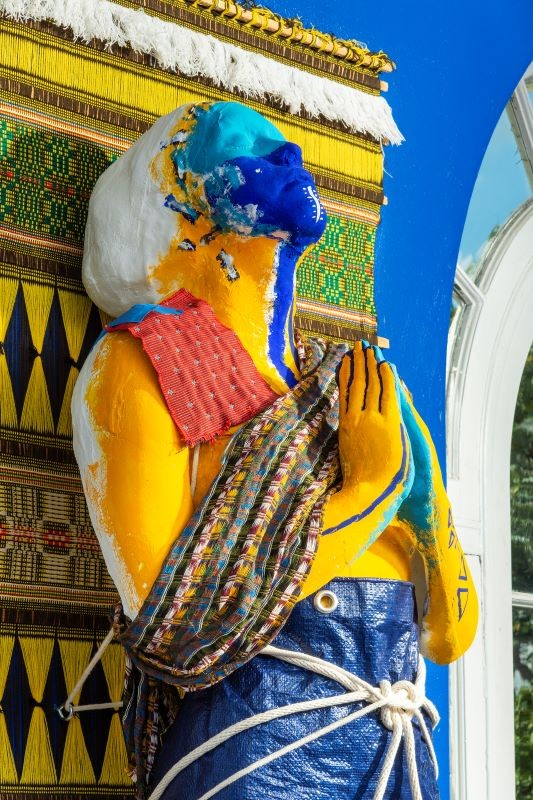 Origins of Devotions (Installation Detail), Dimensions Variable, Plaster, Blue Hurricane tarp as veil, Collected palm boots, Coconuts, Mamey seeds, Avocados from the Deering Estate, Tree snails collected by grandparents, Fragment of US-1, Palm tree leaves posed statue painted shades of blue and yellow