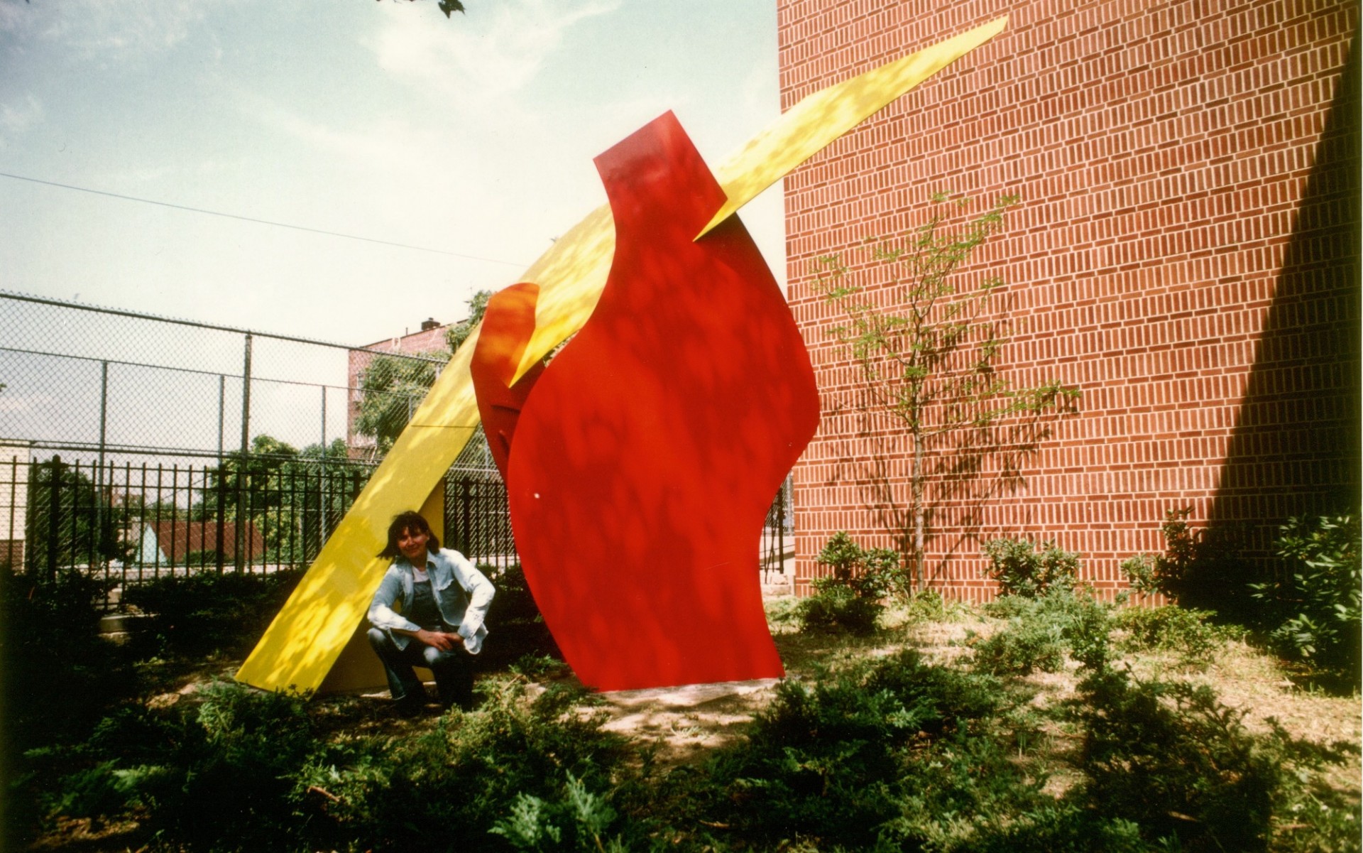 A woman sits next to a large red and yellow abstract sculpture