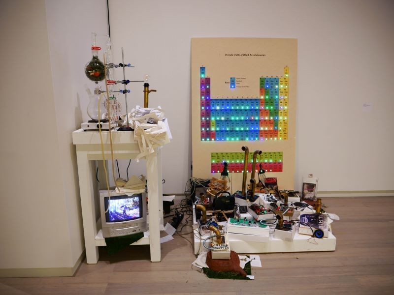 Char Jeré, 'The Community Distillation Project' (books, distillation apparatus, foamboard, weather API, light, circuits, VHS tape, ceramic tree stumps, 2022. Image credit Merry Sun) Art installation