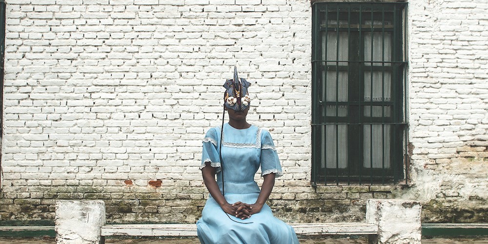 Adama Delphine Fawundu / Tingoi, 2018. © Adama Delphine Fawundu person in blue dress and mask seated outside