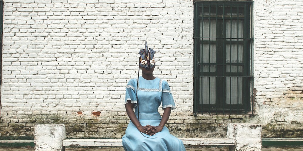 person in blue dress and mask seated outside