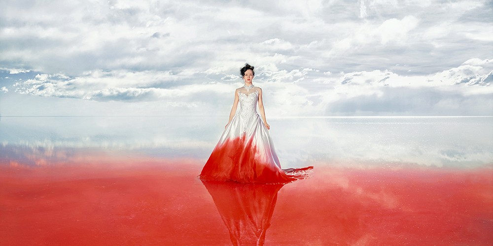 An image of a woman in a white wedding dress with the bottom part red. The background reflects the colors of the dress.