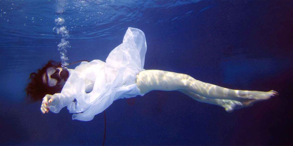 A woman in a white dress submerged in a body of water.