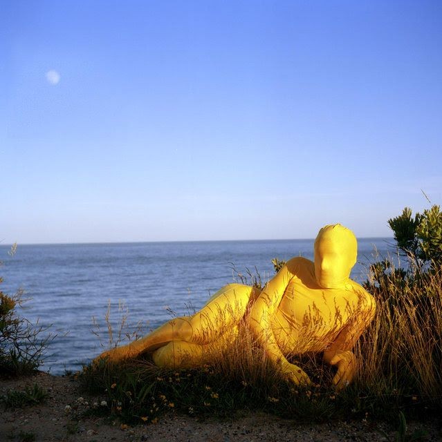 A person in front of the ocean is covered entirely with a yellow suit.