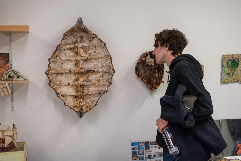 A man leans in to view a sculpture hung on a wall