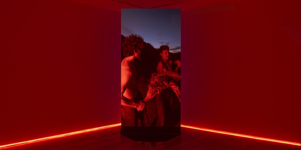 Red room with vertical screen of two people running in the corner. 