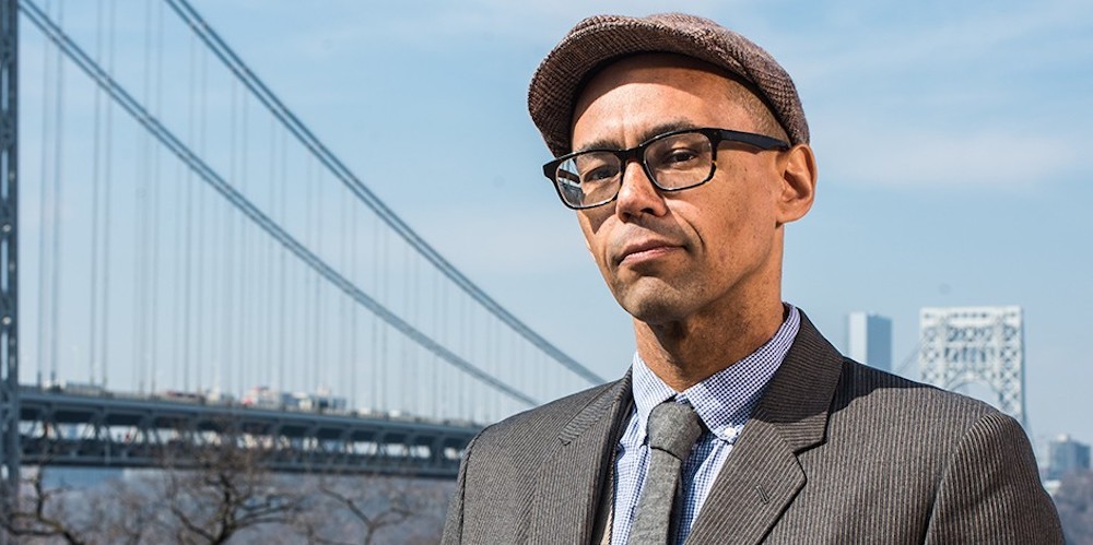 Victor Lavalle stands outside, a bridge in the background. 