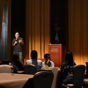 Man stands near a podium speaking to audience. 