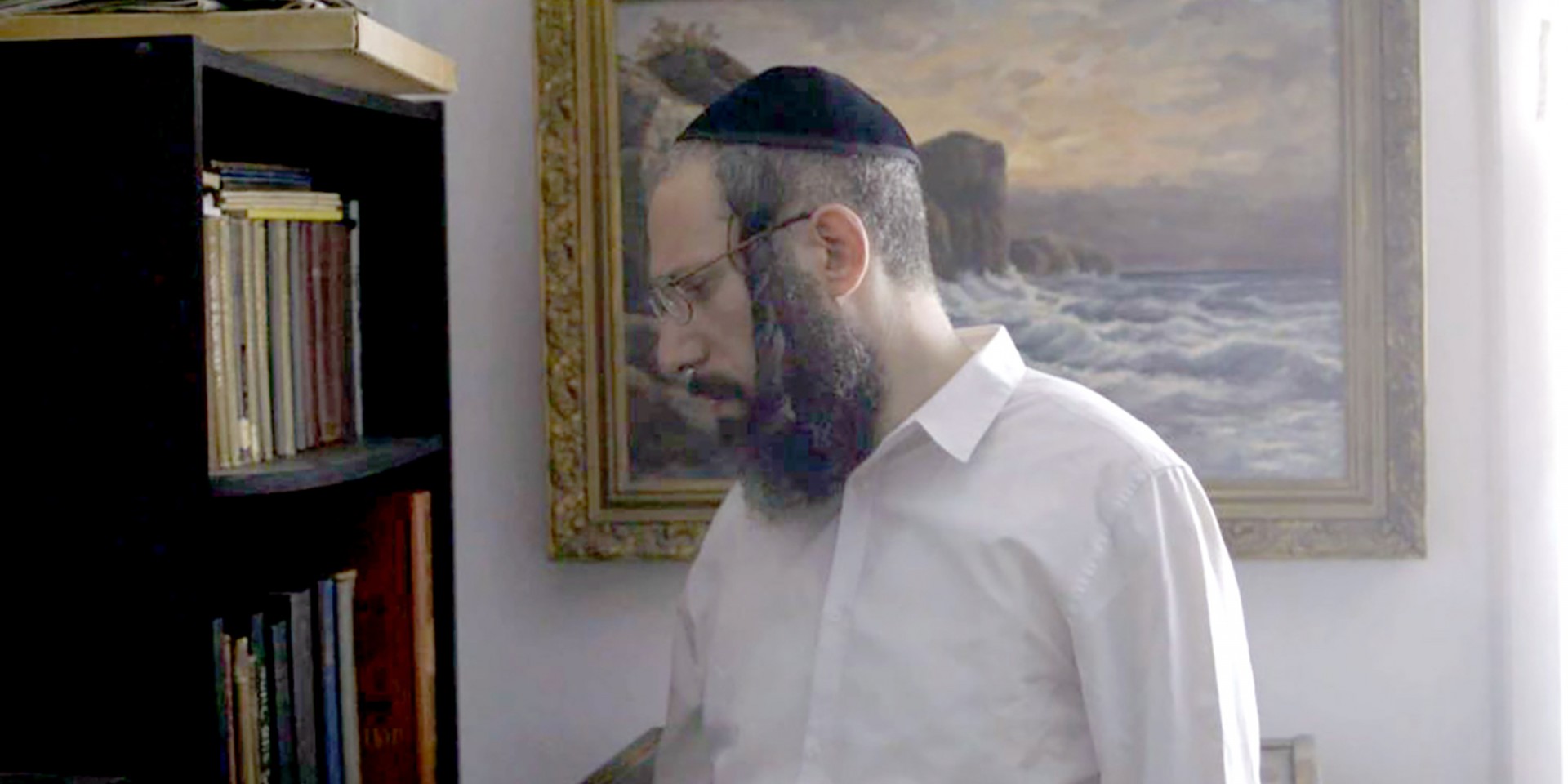 A Hasidic man standing in front of a bookshelf. 