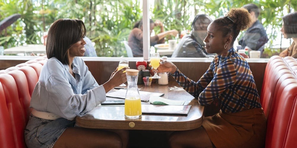 Two Black women speaking to each other in a diner booth