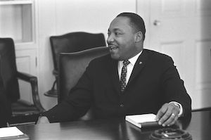 Dr. King at a desk, speaking to someone off camera on his right, smiling.
