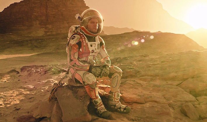 Man in martian suit sitting on a rock. 