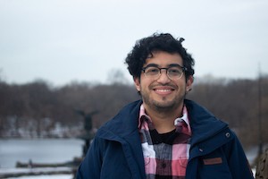 A man with curly hair and glasses smiling in front of a winter backdrop.