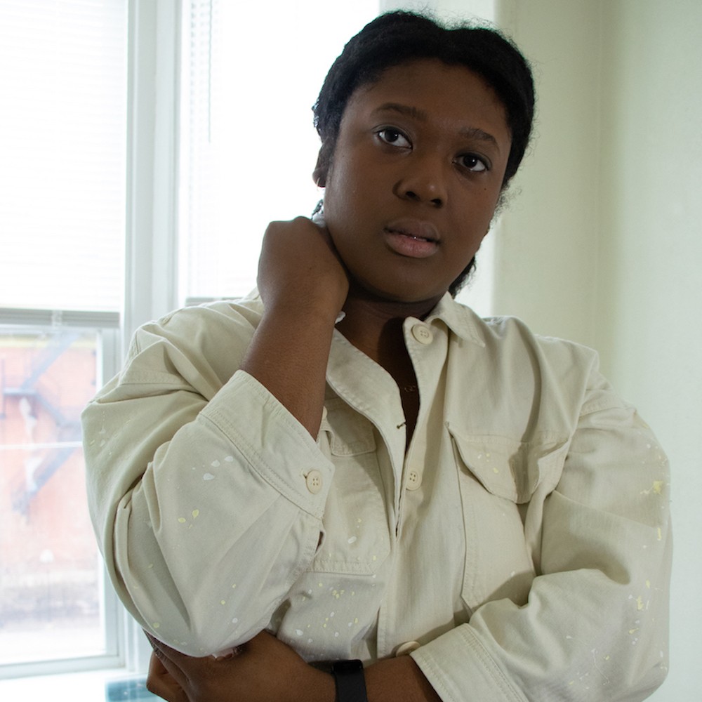 Black woman with folded arms and a beige top. 