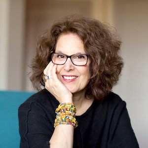 An older white woman smiling with glasses and thick hair. 