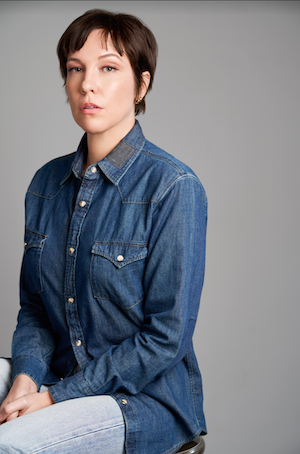White woman with short hair and a denim long sleeve shirt sitting with a serious pose