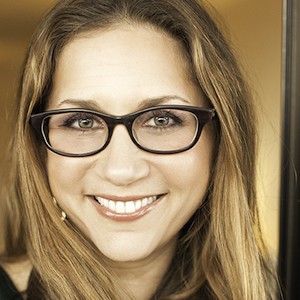 A blond woman with glasses, smiling ear to ear